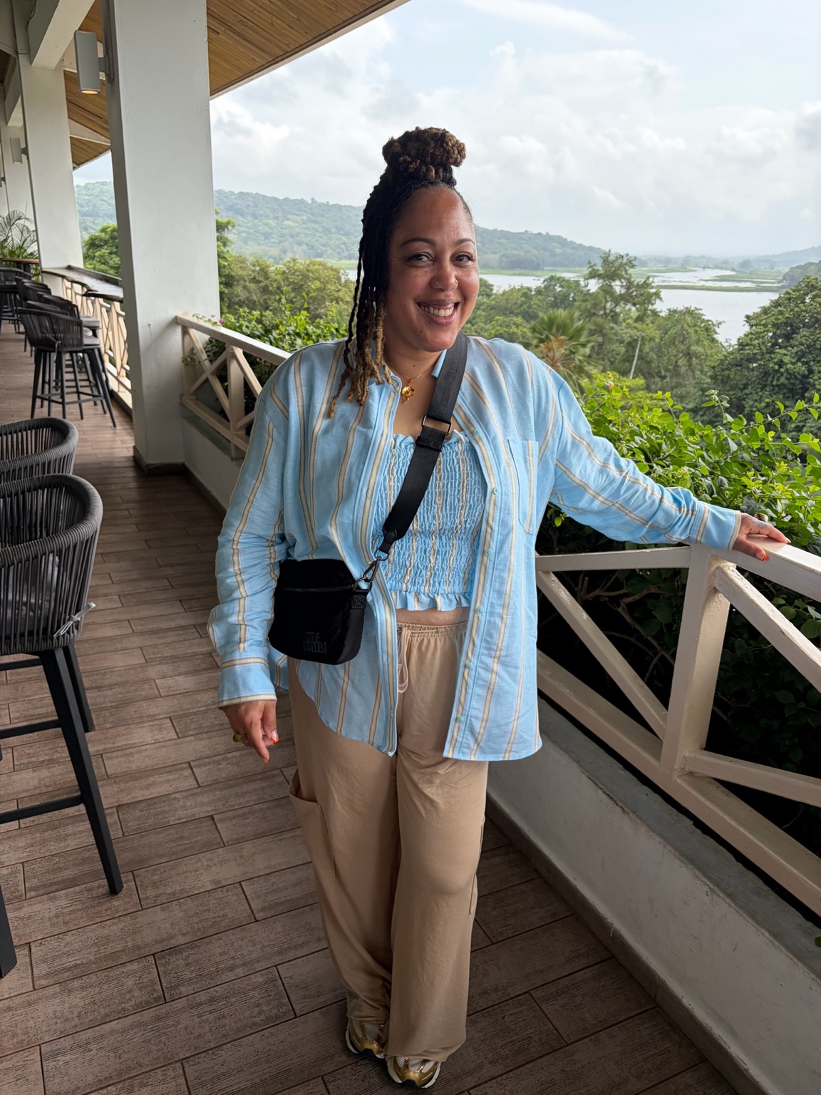 Mesha, your KAM Renewed Wellness coach, smiling on a terrace surrounded by greenery